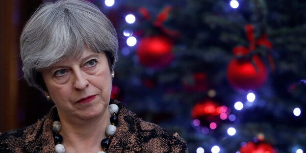 Theresa May blickt grimmig. Hinter ihr Weihnachtsbaumschmuck Theresa May blickt grimmig. Hinter ihr Weihnachtsbaumschmuck