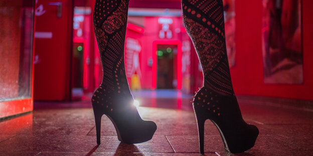 Die Beine einer Frau in Highheels in einem rot beleuchteten Haus Die Beine einer Frau in Highheels in einem rot beleuchteten Haus