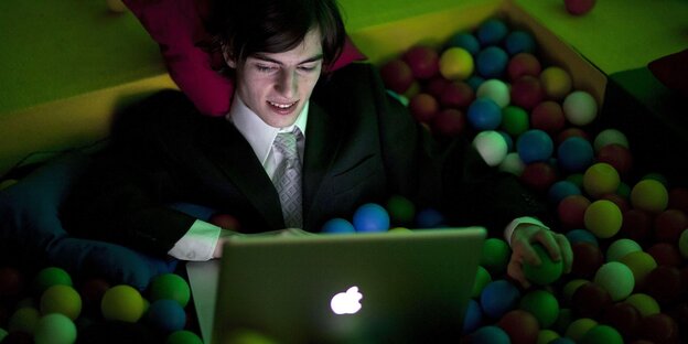 Eine Person sitzt mit Computer in einem Bällebad Eine Person sitzt mit Computer in einem Bällebad