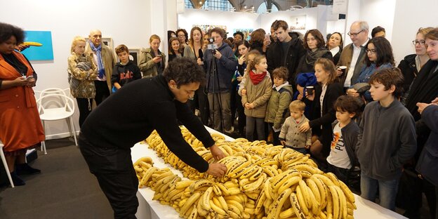 Ganz viele Bananen auf einem Tisch, Leute stehen drumherum