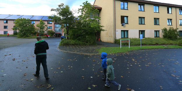 Ein Mann und zwei Kinder gehen über den Hof eines Flüchtlingsheims Ein Mann und zwei Kinder gehen über den Hof eines Flüchtlingsheims