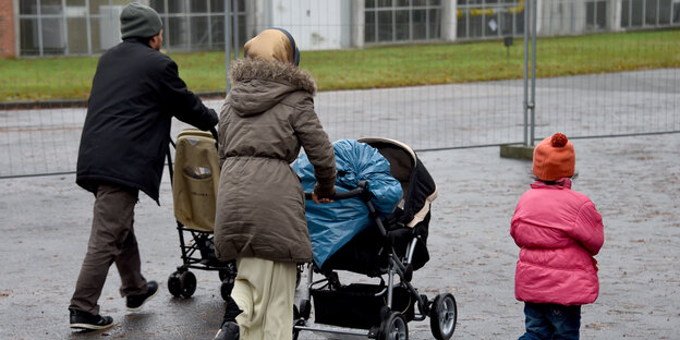 Ein Mann, eine Frau, ein Kind von hinten, Mann und Frau schieben jeweils Kinderwagen Ein Mann, eine Frau, ein Kind von hinten, Mann und Frau schieben jeweils Kinderwagen
