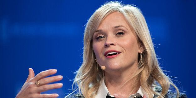 Reese Witherspoon spricht ins Mikro und hebt die Hand hoch Reese Witherspoon spricht ins Mikro und hebt die Hand hoch
