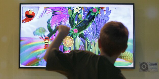 Ein Junge von hinten vor einem Bildschirm, der bunt ist, weil ein Videospiel läuft Ein Junge von hinten vor einem Bildschirm, der bunt ist, weil ein Videospiel läuft