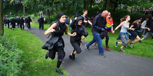Demonstranten rennen in einer Reihe durch eine Grünanlage Demonstranten rennen in einer Reihe durch eine Grünanlage