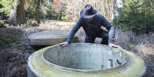 ein Mann beugt sich über einen Betonschacht im Wald ein Mann beugt sich über einen Betonschacht im Wald