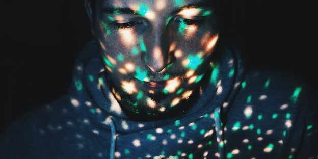 Ein Männergesicht, erleuchtet von bunten Lichtpunkten Ein Männergesicht, erleuchtet von bunten Lichtpunkten