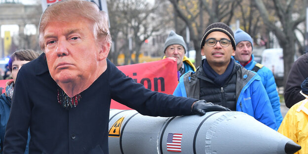 Ein Demonstrant mit riesiger Trump-Maske hält seine linke Hand stolz auf eine Pappmacheé-Atomrakete Ein Demonstrant mit riesiger Trump-Maske hält seine linke Hand stolz auf eine Pappmacheé-Atomrakete
