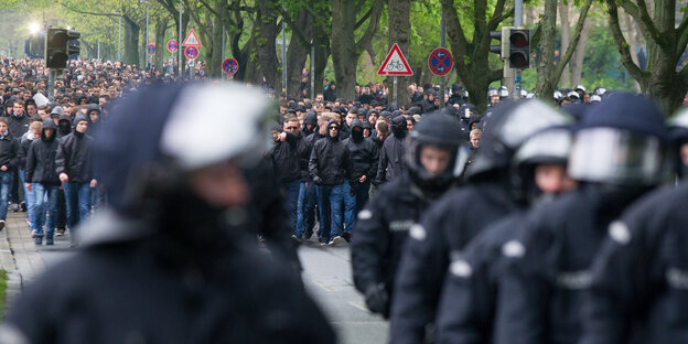 Dunkel gekleidete und teilweise vermummte Fans von Hannover 96 gehen Richtung Stadion und werden dabei von Polizisten eskortiert. Dunkel gekleidete und teilweise vermummte Fans von Hannover 96 gehen Richtung Stadion und werden dabei von Polizisten eskortiert.