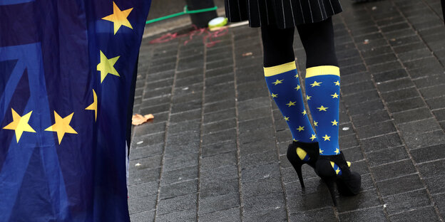 Frauenfüße in schwarzen High-Heels und Söckchen, die mit der EU-Flagge bedruckt sind