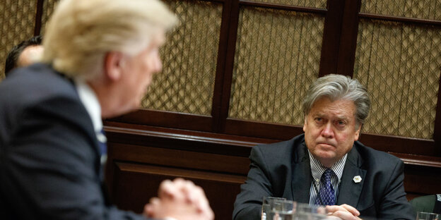 Donald Trumo sitzt an einem Tisch und beugt sich zu Steve Bannon Donald Trumo sitzt an einem Tisch und beugt sich zu Steve Bannon