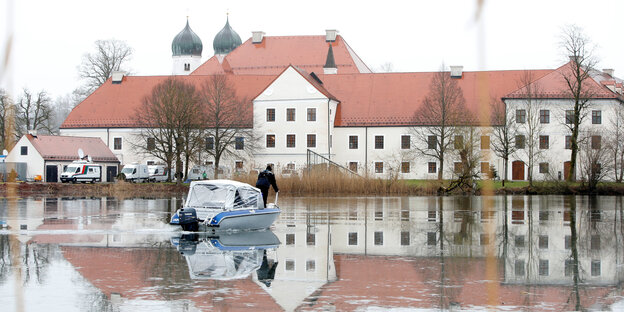 Ein Klostergebäude im Hintergrund, im Vordergrund eine überschwemmte Landschaft und ein Boot Ein Klostergebäude im Hintergrund, im Vordergrund eine überschwemmte Landschaft und ein Boot