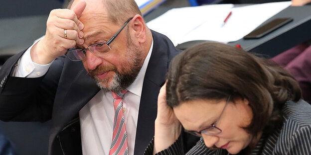 Ein Mann und eine Frau, der Mann fasst sich an die Stirn, die Frau guckt konzentriert nach unten Ein Mann und eine Frau, der Mann fasst sich an die Stirn, die Frau guckt konzentriert nach unten
