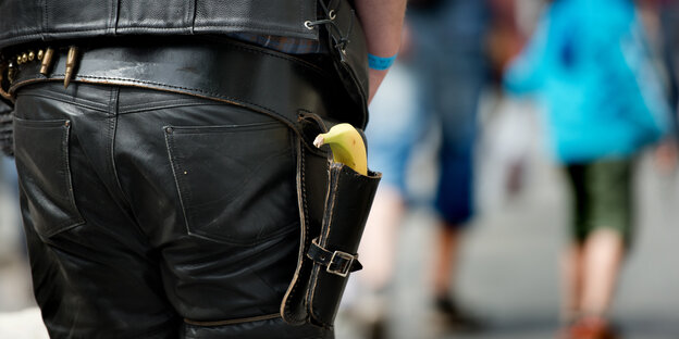 Eine Person in Cowboy-artigem Lederdress hat eine Banane in der Pistolenhalterung hängen. Eine Person in Cowboy-artigem Lederdress hat eine Banane in der Pistolenhalterung hängen.