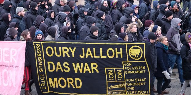 Ein Transpi „Oury Jalloh das war Mord“, dahinter schwarze gekleidete Menschen