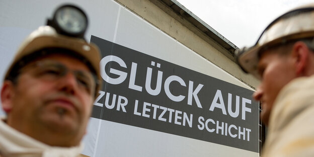 Zwei Bergmänner stehen vor einem Plakat „Glück auf zur letzten Schicht“ Zwei Bergmänner stehen vor einem Plakat „Glück auf zur letzten Schicht“