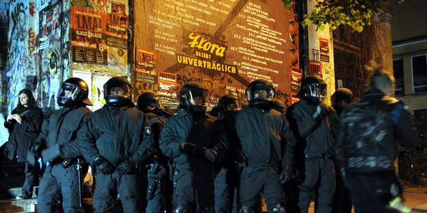 Polizisten mit Helmen und geschlossenem Visier stehen vor der Roten Flora. Polizisten mit Helmen und geschlossenem Visier stehen vor der Roten Flora.