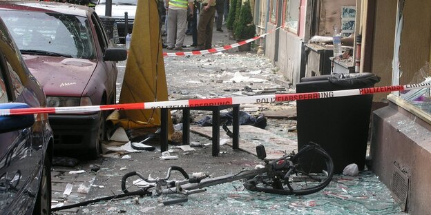 Glasscherben und zerstörte Dinge auf einer Straße, davor Absperrband