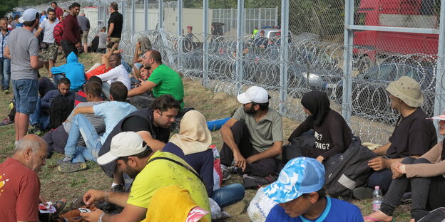 Flüchtlinge sitzen im Gras vor dem Grenzzaun in Röszke Flüchtlinge sitzen im Gras vor dem Grenzzaun in Röszke