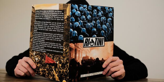 Ein Sammelalbum, auf dessen Cover Polizisten und ein Brand der G20-Proteste abgebildet sind. Das Heft einer schwarz gekleideten Person gehalten. Ein Sammelalbum, auf dessen Cover Polizisten und ein Brand der G20-Proteste abgebildet sind. Das Heft einer schwarz gekleideten Person gehalten.