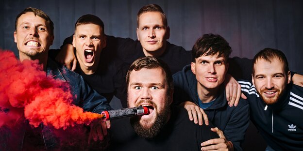 Die sechs Mitglieder von Feine Sahne Fischfilet gucken in die Kamera. Der Sänger hat eine Rauchfackel im Mund Die sechs Mitglieder von Feine Sahne Fischfilet gucken in die Kamera. Der Sänger hat eine Rauchfackel im Mund