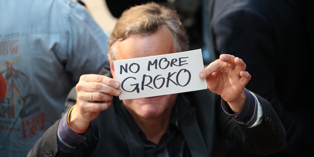 EIn Mann hält einen Zettel mit der Aufschrift "No more Groko" vors Gesicht