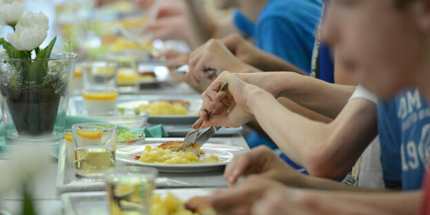 Viele Kinder und Jugendliche sitzen nebeneinander an einem langen Tisch und essen Viele Kinder und Jugendliche sitzen nebeneinander an einem langen Tisch und essen