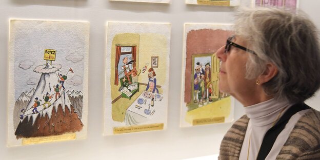 Eine Frau sieht sich bunte Bilder an, die an einer Wand hängen Eine Frau sieht sich bunte Bilder an, die an einer Wand hängen