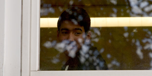 Ein Junge mit dunklen Haaren und dunklen Augenbrauen blickt aus einem Fenster. Ein Junge mit dunklen Haaren und dunklen Augenbrauen blickt aus einem Fenster.