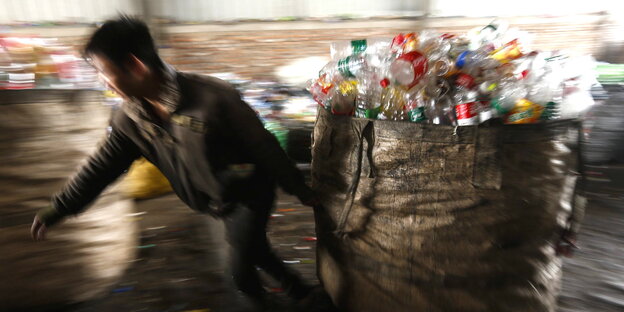 Ein Mann zieht einen großen Sack mit Plastikflaschen Ein Mann zieht einen großen Sack mit Plastikflaschen