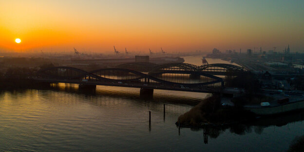 Die untergehende Sonne spiegelt sich in der Elbe. Es sind die Shiloutten der Elbbrücken und Container-Kräne zu sehen. Die untergehende Sonne spiegelt sich in der Elbe. Es sind die Shiloutten der Elbbrücken und Container-Kräne zu sehen.