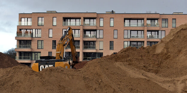 Ein Bagger steht vor einem neu gebauten Mehrfamilienhaus. Ein Bagger steht vor einem neu gebauten Mehrfamilienhaus.