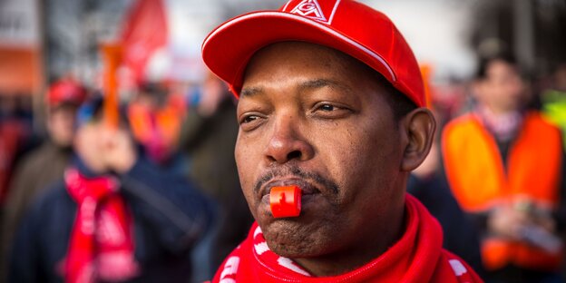 Mann mit roter Kappe und einer Trillerpfeife im Mund Mann mit roter Kappe und einer Trillerpfeife im Mund