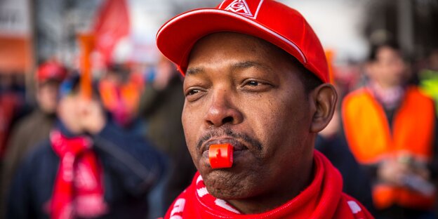 Mann mit roter Kappe und einer Trillerpfeife im Mund