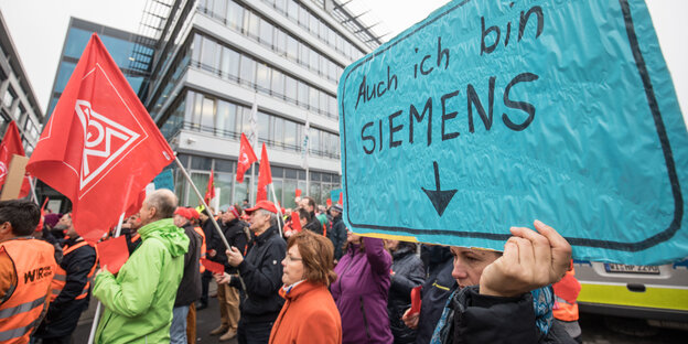 Demonstrationsteilnehmer mit Gewerkschaftsfahnen vor einem Haus, einer hält ein Schild hoch auf dem "Auch ich bin Siemens" steht Demonstrationsteilnehmer mit Gewerkschaftsfahnen vor einem Haus, einer hält ein Schild hoch auf dem "Auch ich bin Siemens" steht