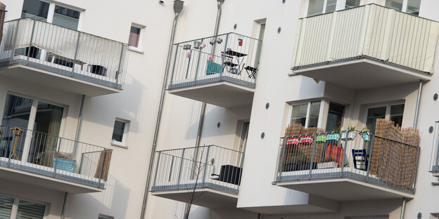 Eine Hauswand mit Balkonen. Auf einem Balkon stehen Tische, ein anderer ist mit einem Sichtschutz umhüllt.