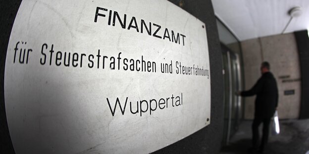 ein Schild mit der Aufschrift "Finanzamt für Steuerstrafsachen und Steuerfahndung - Wuppertal", im Hintergrund betritt ein Mann ein Gebäude ein Schild mit der Aufschrift "Finanzamt für Steuerstrafsachen und Steuerfahndung - Wuppertal", im Hintergrund betritt ein Mann ein Gebäude