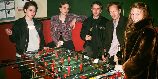 Eine Gruppe junger Männer und Frauen stehen um ein Tischfußball-Spiel, alle haben eine Flasche Bier in der Hand Eine Gruppe junger Männer und Frauen stehen um ein Tischfußball-Spiel, alle haben eine Flasche Bier in der Hand