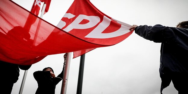 Menschen halten eine SPD-Fahne, die aufgezogen werden soll Menschen halten eine SPD-Fahne, die aufgezogen werden soll