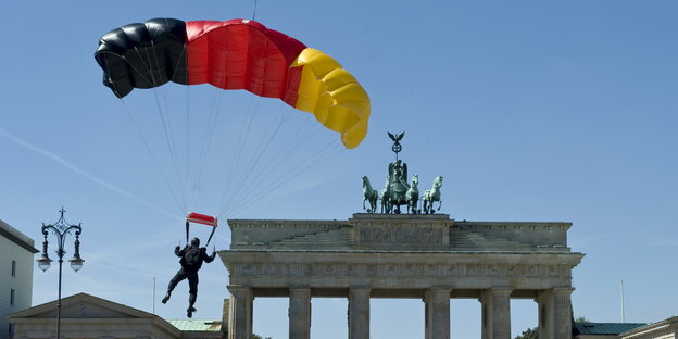 ein Fallschirmspringer mit einem schwarz-rot-goldenen Schirm landet vor dem Brandenburger Tor ein Fallschirmspringer mit einem schwarz-rot-goldenen Schirm landet vor dem Brandenburger Tor