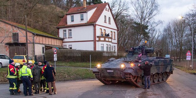 Ein Panzer steht vor einer Gruppe Feuerwehrleute