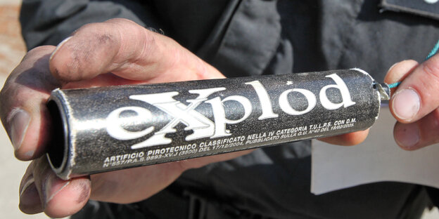 Zwei Hände, die einen schwarzen Böller mit dem weißen Schriftzug "Explod" halten. Zwei Hände, die einen schwarzen Böller mit dem weißen Schriftzug "Explod" halten.