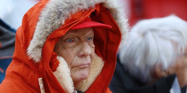 Niki Lauda trägt über einem roten Käppi und die Mütze einer roten Winterjacke Niki Lauda trägt über einem roten Käppi und die Mütze einer roten Winterjacke