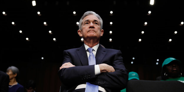 Jerome Powell sitzt mit verschränkten Armen, Lichterreihen an der Decke über ihm Jerome Powell sitzt mit verschränkten Armen, Lichterreihen an der Decke über ihm