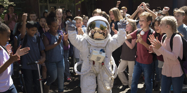Viele Kinder stehen um einen Jungen im Astronautenanzug und klatschen Viele Kinder stehen um einen Jungen im Astronautenanzug und klatschen