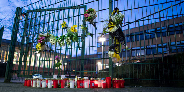 Ein Zaun vor einer Schule. Mit Grablichtern und Blumen