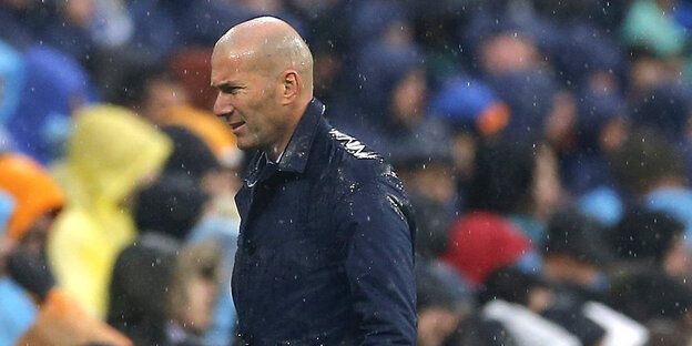 Ein Mann im Regen vor einer Tribüne voller Menschen Ein Mann im Regen vor einer Tribüne voller Menschen