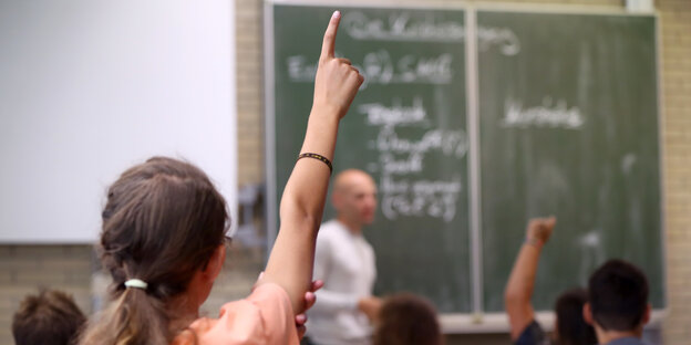 Kinder in einer Schulklasse melden sich. Der Lehrer steht vor einer beschriebenen Tafel. Kinder in einer Schulklasse melden sich. Der Lehrer steht vor einer beschriebenen Tafel.