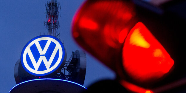 ein rotes Ampellicht leuchtet vor einem VW-Symbol vor dunkelblauem Abendhimmel ein rotes Ampellicht leuchtet vor einem VW-Symbol vor dunkelblauem Abendhimmel