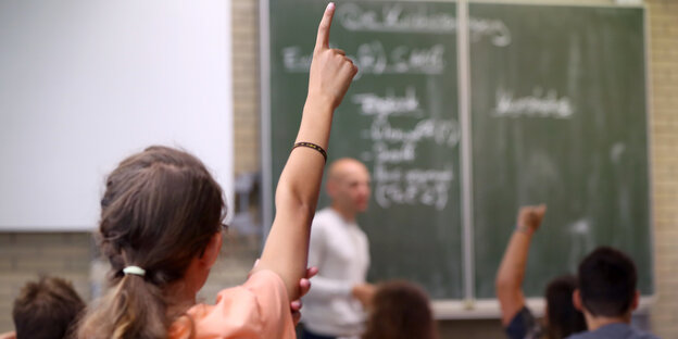 Kinder sitzen vor einer Tafel und heben die Hand Kinder sitzen vor einer Tafel und heben die Hand